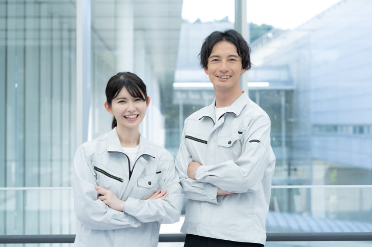 物流・製造業界で使用するような作業着を着た男女が笑顔でそれぞれ腕組をしている写真